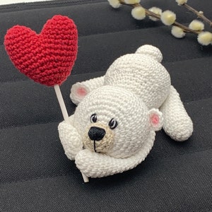 May include: A white crocheted polar bear holding a red crocheted heart on a stick.