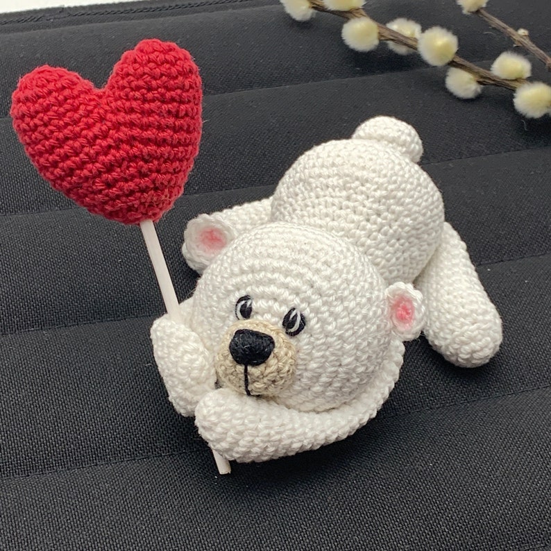 May include: A white crocheted polar bear holding a red crocheted heart on a stick.