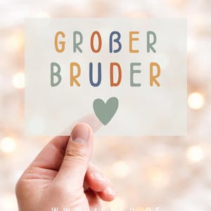 Könnte beinhalten: Eine rechteckige Karte, die in einer Hand gehalten wird, zeigt die Worte "GROBER BRUDER" in farbenfrohen, verspielten Buchstaben, mit einem grünen Herz darunter. Die Karte enthält auch die Website-Adresse "WWW.JEKLU.DE".