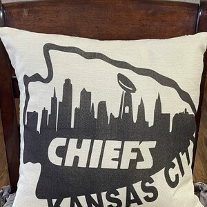 May include: A white pillow with a black silhouette of the Kansas City skyline and the words "CHIEFS KANSAS CITY".