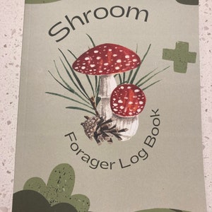 Może przedstawiać: Zielony i brązowy dziennik z tekstem "Shroom Forager Log Book" i rysunkiem dw&oacute;ch czerwono-białych grzyb&oacute;w.