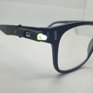 May include: Black rectangular glasses with a built-in LED light on the side of the frame.