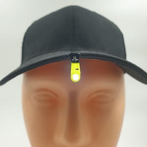 Puede incluir: Gorra de béisbol negra con una luz LED amarilla neón adjunta a la visera. La luz es rectangular y tiene una pequeña luz blanca en el extremo. La gorra está hecha de tela oscura.