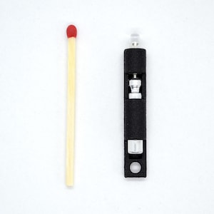 May include: A small black and silver torch with a red matchstick for scale.