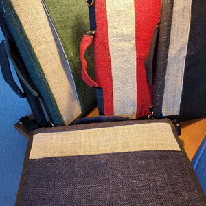 May include: Four different colored zippered bags made of woven fabric. The bags are lined up in a row on a wooden surface. The bags are all the same size and shape. The bags are made of a natural fiber, such as jute or hemp.