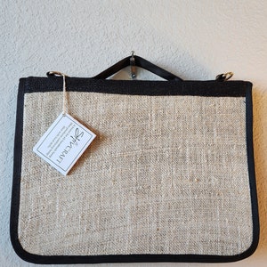 May include: A black and beige jute tote bag with a black leather handle and a small white tag that reads "SHIVCRAFT A brand for all handmade herp Bilet products combining the best of nature with local skill".