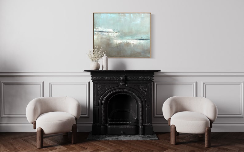 May include: A black fireplace with a white mantel and two white chairs in front of it. A framed abstract painting with blue, white, and brown colors hangs above the mantel.