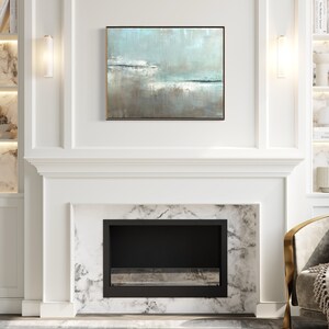 May include: A white fireplace with a black firebox and a marble surround. The fireplace is flanked by white built-in shelves with marble backs and gold accents. A light blue abstract painting hangs above the fireplace. A gold and white armchair with a gray throw and pillow sits in front of the fireplace.