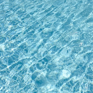 Puede incluir: Primer plano de agua azul clara y ondulante. La superficie está texturizada con suaves olas y reflejos, creando un efecto brillante. El color del agua varía de azul claro a azul profundo, lo que sugiere profundidad y claridad.