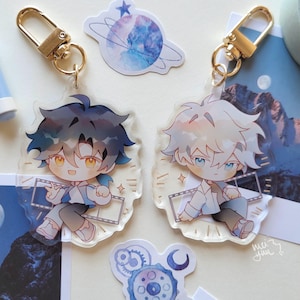 May include: Two anime-style acrylic keychains with gold-colored clasps. Each keychain features a cartoon character with spiky hair, one with dark blue and the other with white hair. The characters are holding film strips.