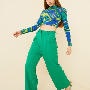 Pu&ograve; includere: Una donna indossa un top corto a maniche lunghe con stampa astratta blu e verde e pantaloni larghi verdi.