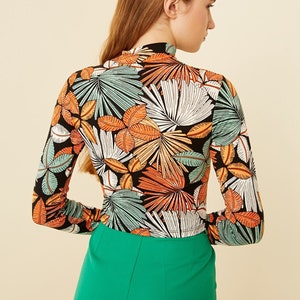 May include: A black long-sleeved shirt with a tropical leaf print in shades of green, orange, and white. The shirt has a mock neck and a fitted silhouette.