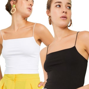 May include: Two women wearing white and black spaghetti strap tank tops. The woman on the left is wearing yellow trousers and the woman on the right is wearing white trousers.