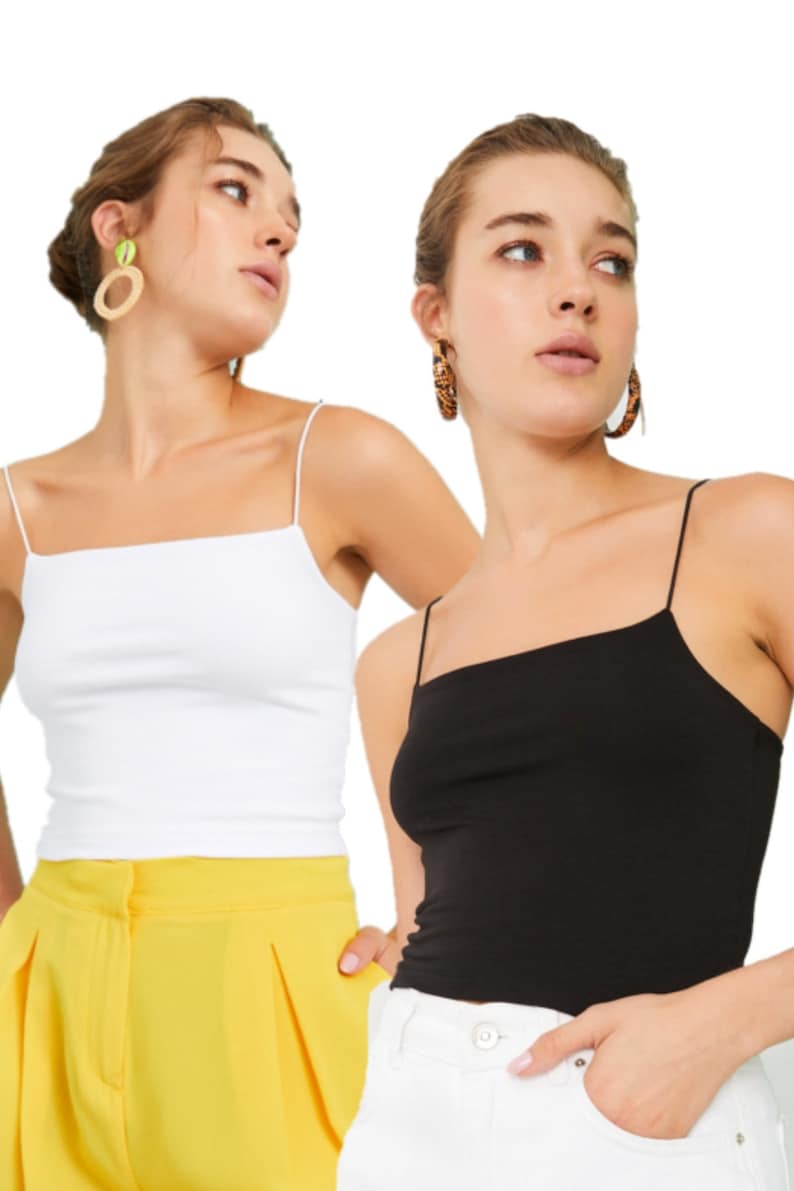 May include: Two women wearing white and black spaghetti strap tank tops. The woman on the left is wearing yellow trousers and the woman on the right is wearing white trousers.