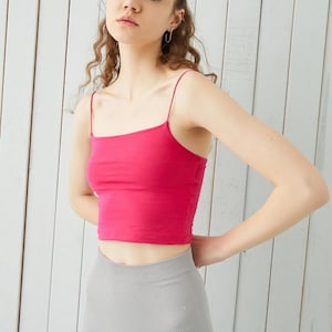 May include: A woman wearing a pink tank top and grey leggings. The tank top has thin straps and a square neckline.
