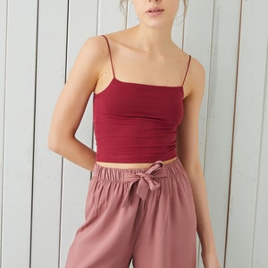 May include: A woman is wearing a burgundy tank top and dusty rose wide-leg trousers with a drawstring waist.