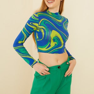 Pu&ograve; includere: Un top corto a maniche lunghe blu e verde con una stampa astratta a spirale. Il top &egrave; abbinato a pantaloni verdi a vita alta.