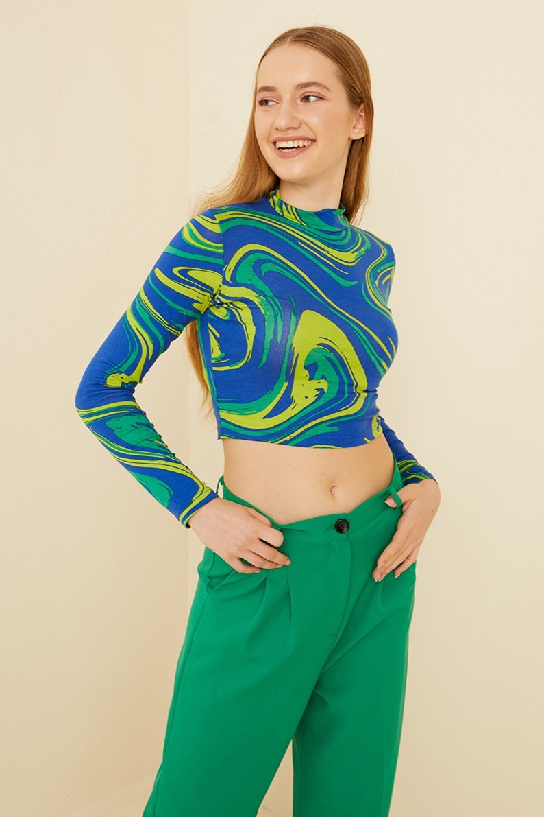 Pu&ograve; includere: Un top corto a maniche lunghe blu e verde con una stampa astratta a spirale. Il top &egrave; abbinato a pantaloni verdi a vita alta.