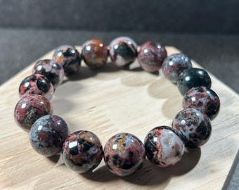 May include: A bracelet made of round, multi-colored, speckled beads. The beads are a mix of red, black, white, and brown.