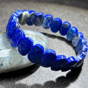 May include: A blue lapis lazuli bracelet. The bracelet is composed of oval-shaped, polished stones in varying shades of blue, strung together to form a flexible band. The stones have a natural, slightly mottled appearance.