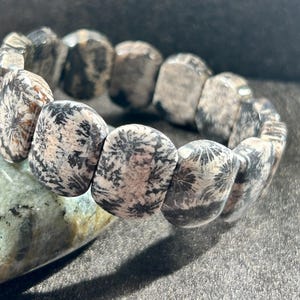 Könnte beinhalten: Ein Armband aus schwarz-weiß gemustertem Stein mit floralem Design. Das Armband besteht aus runden, flachen Steinen, die aneinandergereiht sind.
