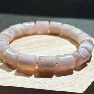 Puede incluir: Un brazalete de ágata rosa y blanca con cuentas cilíndricas. El brazalete está hecho de piedra natural y tiene un acabado pulido.
