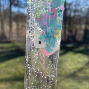 May include: A clear glass tube filled with a glittery liquid, containing a small white unicorn figurine and colorful confetti.