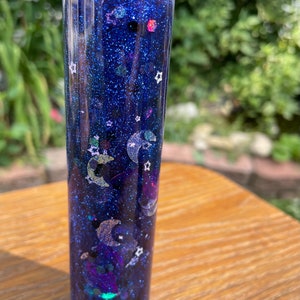 May include: A clear glass bottle filled with a blue glitter liquid and various silver and white glitter shapes, including stars and crescent moons.