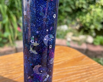 May include: A clear glass bottle filled with a blue glitter liquid and various silver and white glitter shapes, including stars and crescent moons.