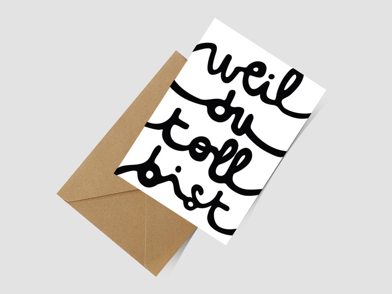May include: A white greeting card with black handwritten cursive text that reads "weil du toll bist" positioned diagonally next to a brown kraft paper envelope. The card features a clean design with bold, flowing lettering across the front surface.