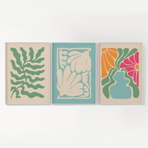May include: Three framed prints with abstract floral designs. The first print features a green leafy design on a beige background. The second print features a cream-colored floral design on a light blue background. The third print features a vase with orange and pink flowers on a beige background.