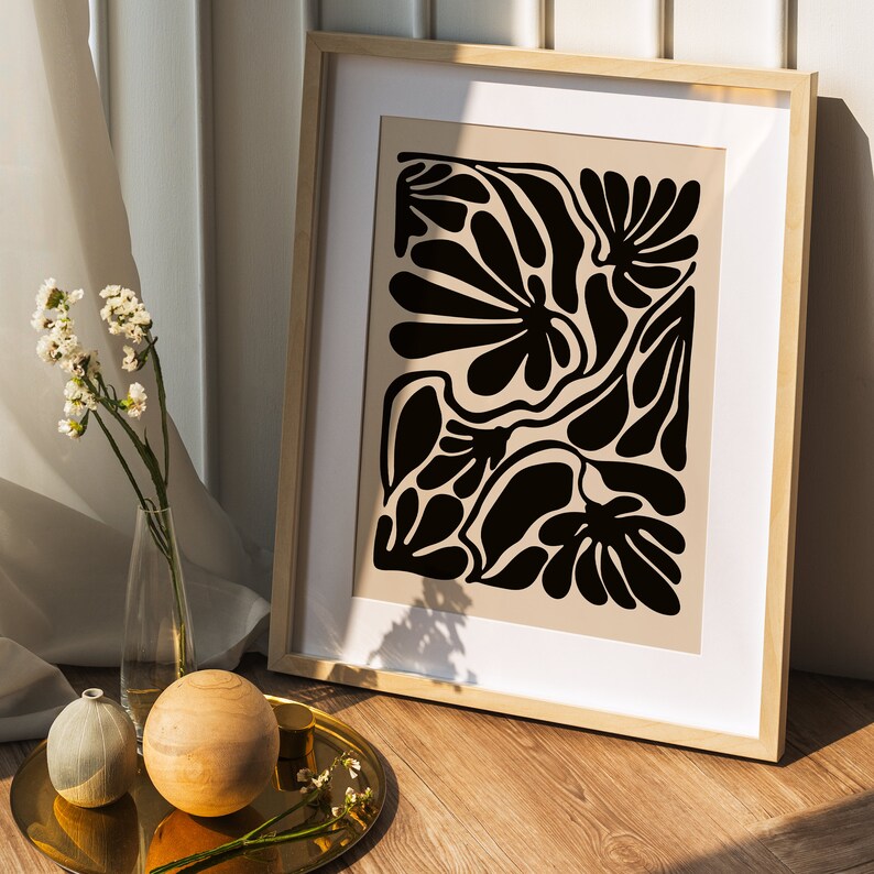 May include: A framed print with a black and white abstract design of stylized flowers. The print is in a light wood frame and is hanging on a white wall.