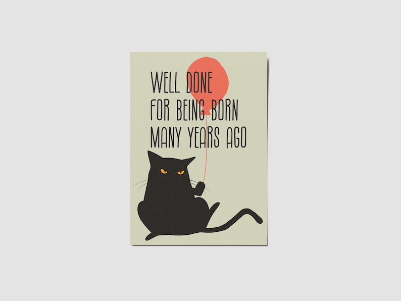 May include: A rectangular greeting card with a light beige background featuring a black cat with yellow eyes holding a red balloon. The text reads: WELL DONE FOR BEING BORN MANY YEARS AGO. The cat is depicted in a seated position with its tail extended.
