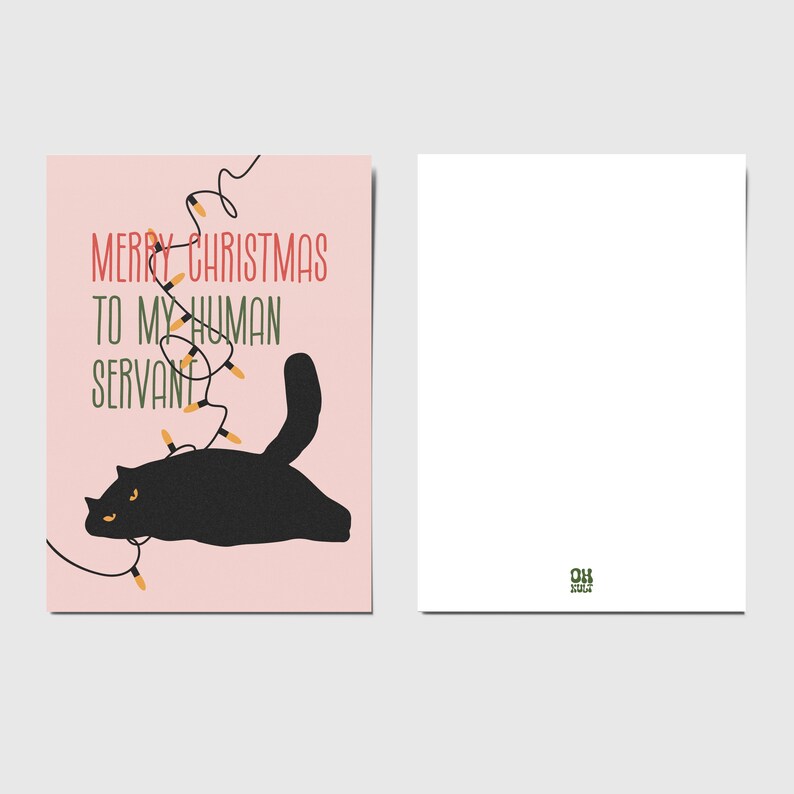May include: A rectangular greeting card with a light pink background featuring a black cat tangled in a string of orange Christmas lights. The text reads MERRY CHRISTMAS TO MY HUMAN SERVANT in red and green. The back is plain white with a small green logo.