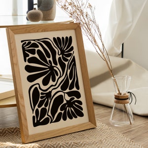 May include: A framed print with a black and white abstract design of organic shapes and leaves. The print is on a cream background and has a wooden frame.