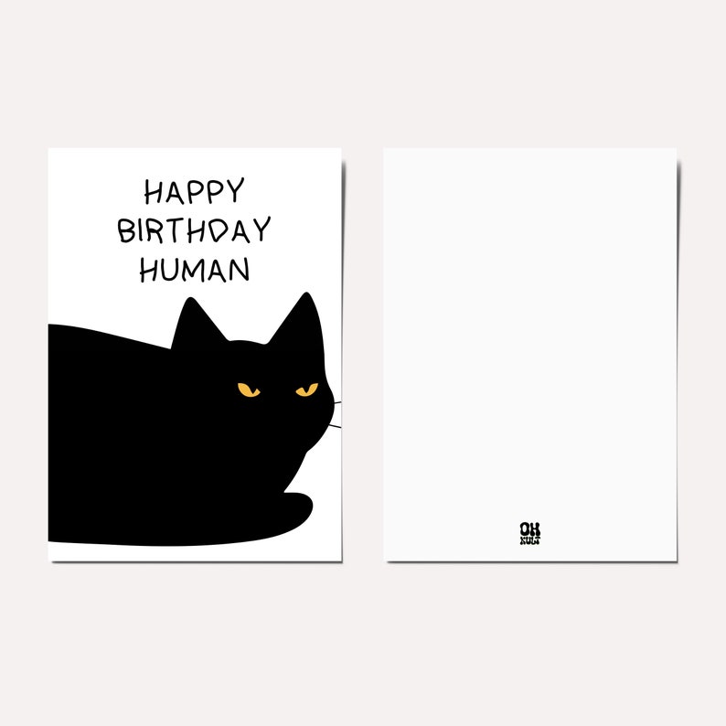 May include: A black cat with yellow eyes looking to the right. The cat is lying down and the text "HAPPY BIRTHDAY HUMAN" is above the cat.
