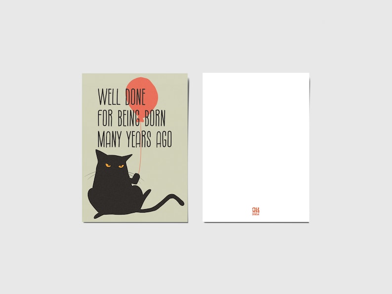 May include: A rectangular greeting card featuring a black cat with orange eyes holding a red balloon. The text reads, "WELL DONE FOR BEING BORN MANY YEARS AGO." The card is shown from the front and the back, with a small red logo on the back side.