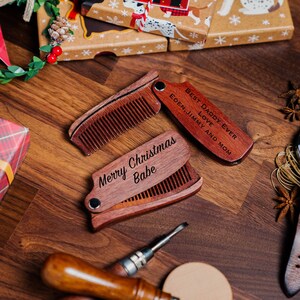 K&ouml;nnte beinhalten: Zwei Holz-Taschenkamm mit gravierten Botschaften. Ein Kamm tr&auml;gt die Aufschrift "Best Daddy Ever" und der andere "Merry Christmas Babe".