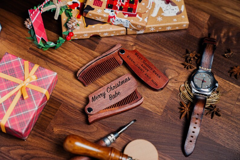K&ouml;nnte beinhalten: Zwei Holz-Taschenkamm mit gravierten Botschaften. Ein Kamm tr&auml;gt die Aufschrift "Best Daddy Ever" und der andere "Merry Christmas Babe".