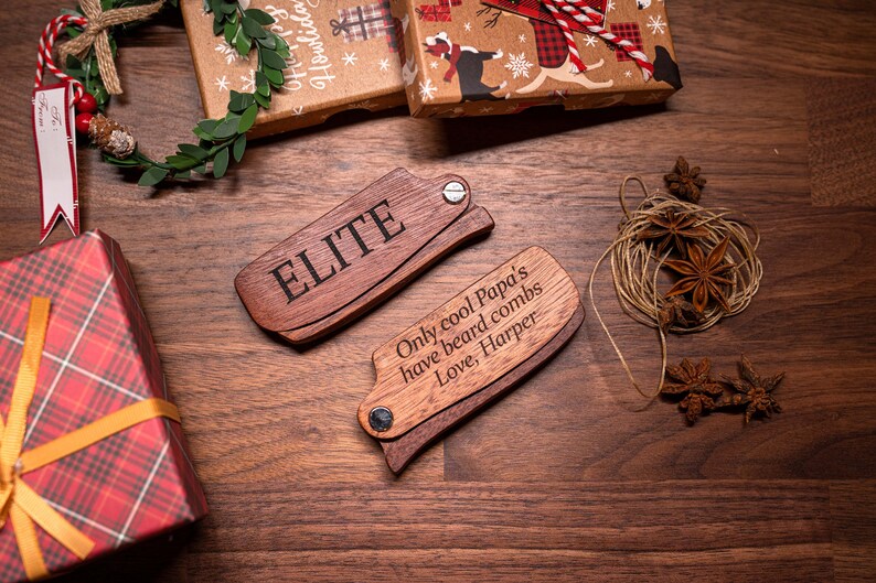 K&ouml;nnte beinhalten: Zwei Holz-Bartscheider mit einer personalisierten Nachricht. Der obere Kamm sagt "ELITE" und der untere Kamm sagt "Nur coole Papas haben Bartscheider. Liebe, Harper".