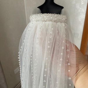 May include: A white bridal veil with a beaded trim and scattered beads throughout the tulle.