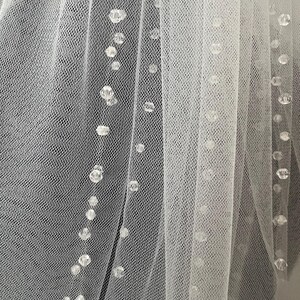 Puede incluir: Velo de novia blanco con un delicado patr&oacute;n de peque&ntilde;as cuentas transparentes.