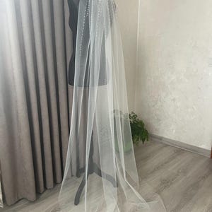 Puede incluir: Un velo de novia largo de tul blanco con ribete de cuentas. El velo est&aacute; drapeado sobre un maniqu&iacute; y cae al suelo.