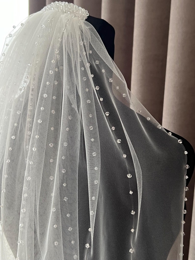 Puede incluir: Un velo de novia blanco de una sola capa con un borde de cuentas. El velo est&aacute; hecho de tul suave y presenta un delicado patr&oacute;n de peque&ntilde;as cuentas transparentes.