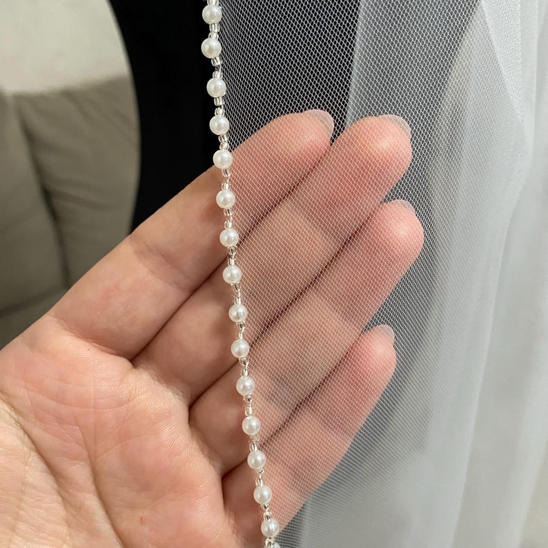 May include: A white bridal veil with a pearl trim. The veil is made of soft tulle and has a delicate, romantic look.