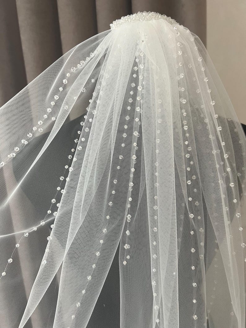 Puede incluir: Un velo de novia blanco de una sola capa de tul con un borde de cuentas. El velo est&aacute; decorado con peque&ntilde;as cuentas espaciadas uniformemente.