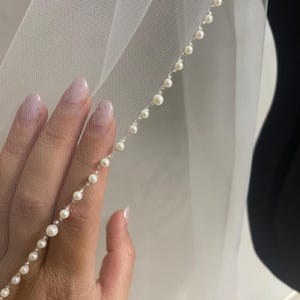 May include: A white bridal veil with a single row of pearl trim along the edge.