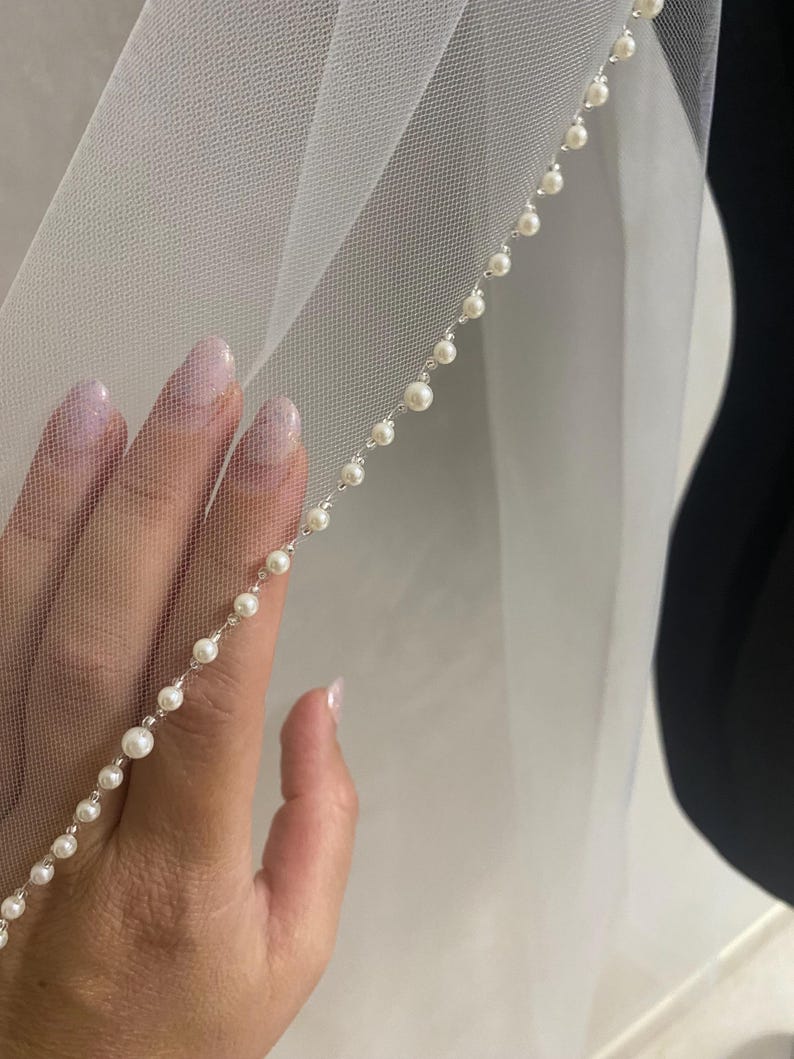 May include: A white bridal veil with a single row of pearl trim along the edge.