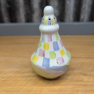 May include: A ceramic salt shaker with a bulbous body and a narrow neck. The shaker is painted white with a colorful patchwork design of blue, yellow, pink, and green squares. The neck has small holes for dispensing salt.