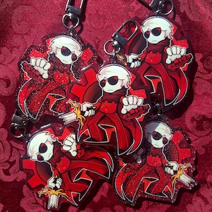 Peut inclure: Porte-clés représentant un personnage de dessin animé rouge et noir avec des cheveux blancs, des lunettes de soleil et une épée. Le personnage est placé sur un engrenage rouge. Chaque porte-clés a un fermoir argenté.